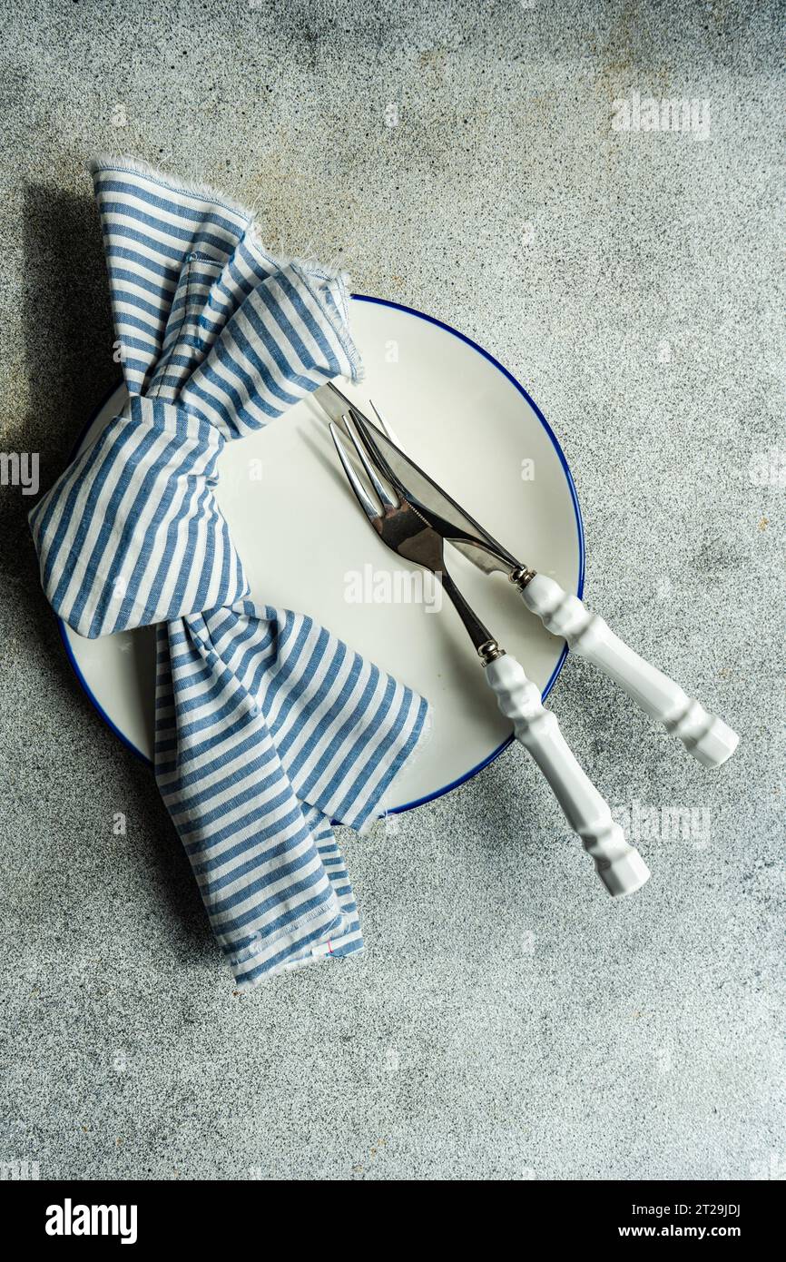 Top view of minimalistic rustic table setting with white plate cutlery and striped napkin on gray surface Stock Photo