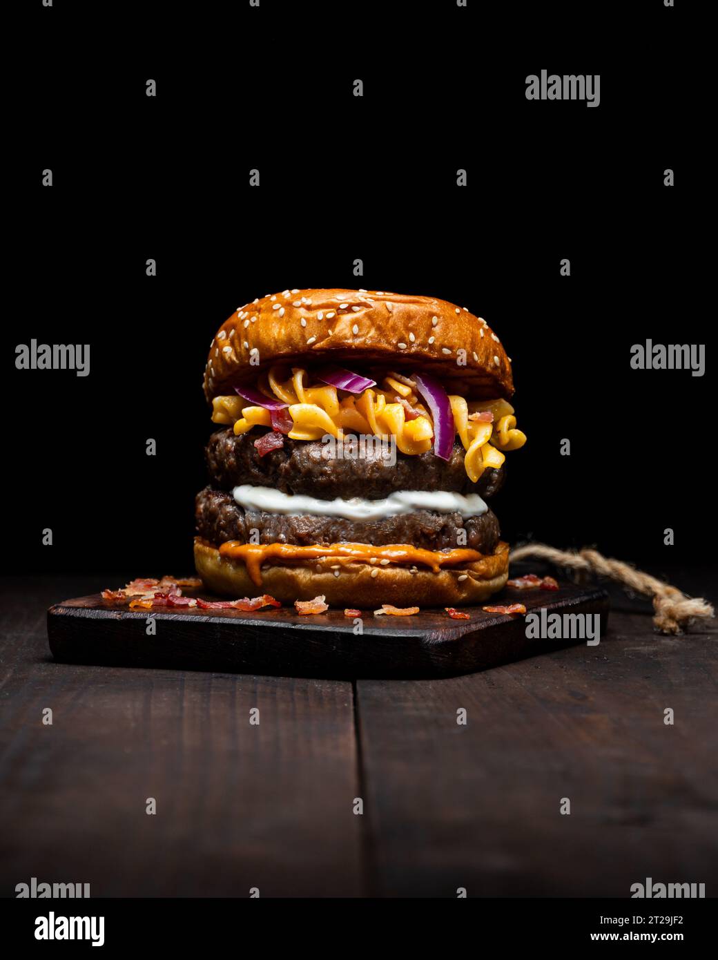 Hamburger with macaroni and cheese placed on wooden tray on table against dark background Stock Photo