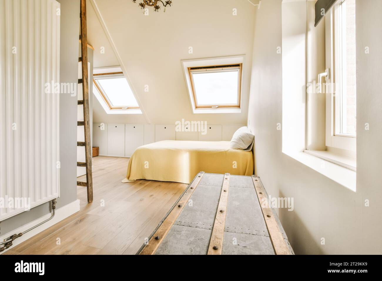 https://c8.alamy.com/comp/2T29KK9/interior-of-attic-bedroom-with-yellow-cozy-bed-and-metallic-treasure-box-by-white-walls-and-windows-in-modern-house-2T29KK9.jpg