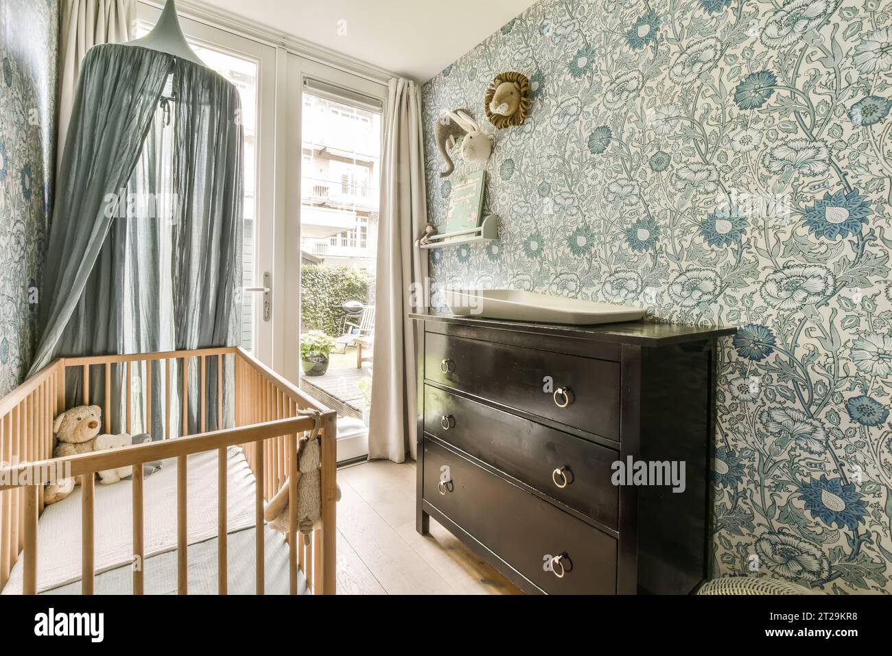 Interior of small nursery with wooden crib and dresser by window at