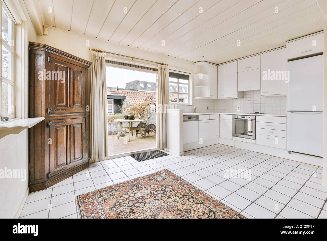 Open plan kitchen with white cabinets and appliances by large window in ...