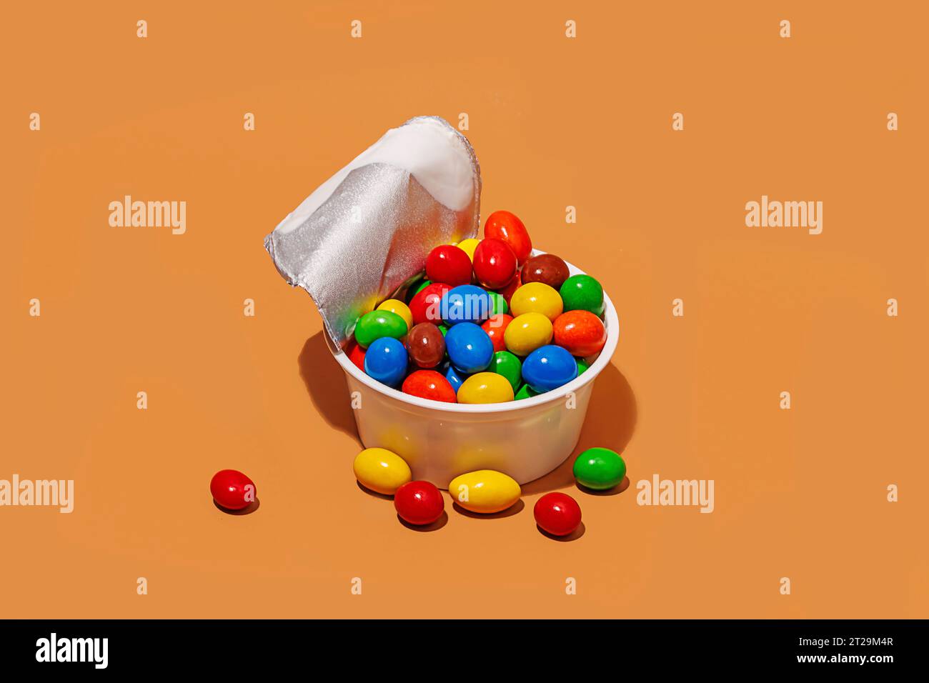 High angle of opened yogurt container filled with colored candies