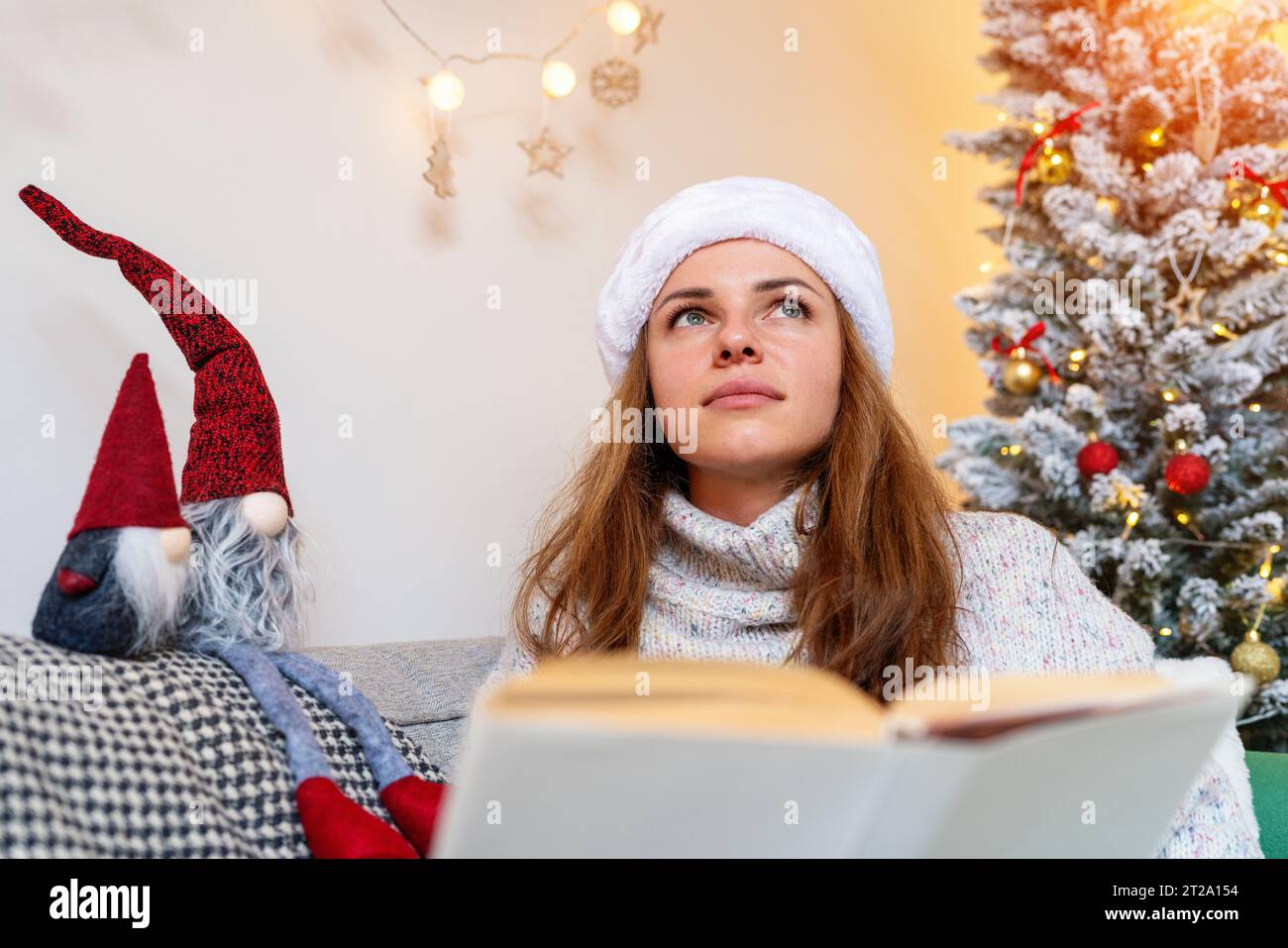 Infantility and childhood dreams. Adult woman dreaming and imagining while reading Christmas fairy tale. Stock Photo