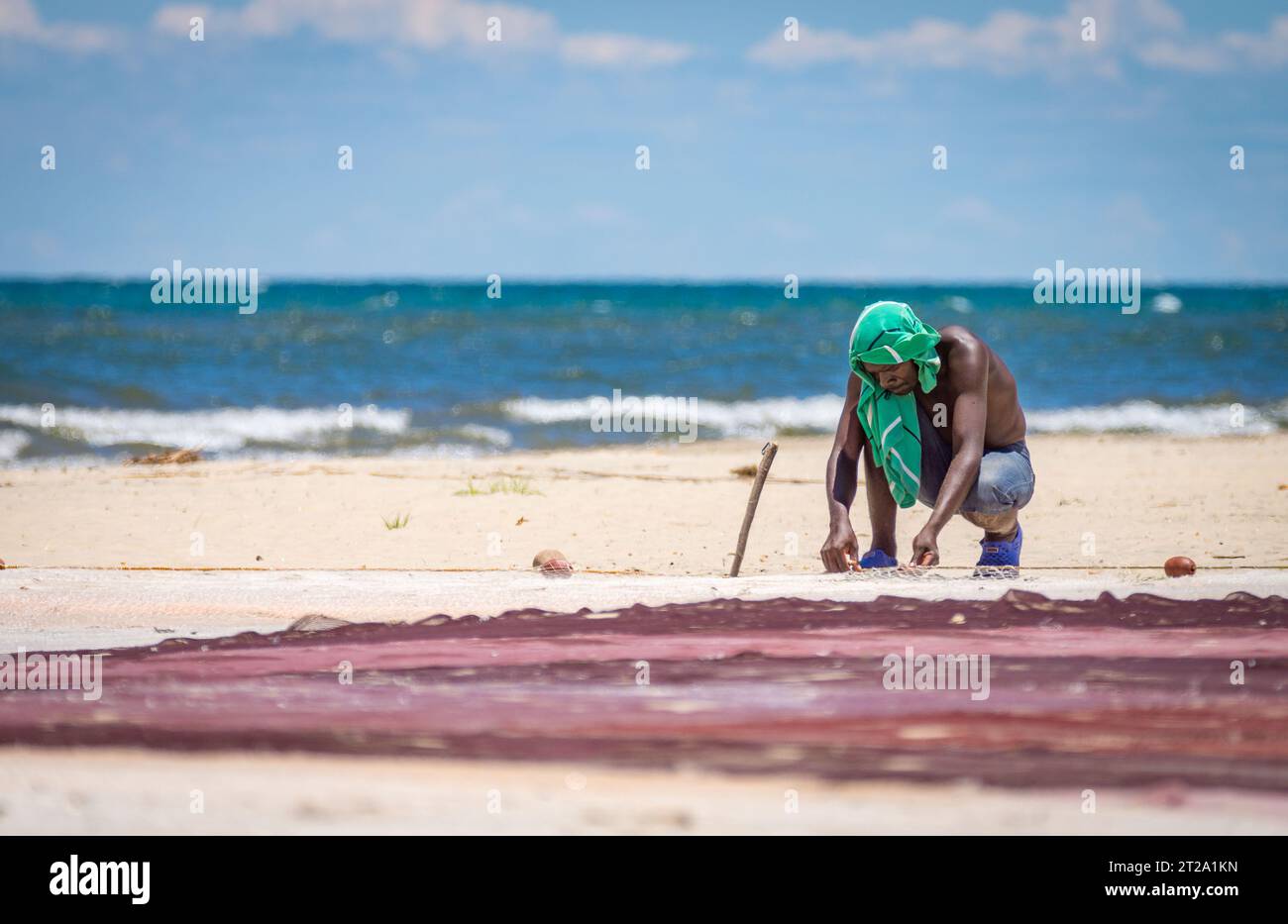 A man on the shore of Lake Malawi mends his fishing net in the midday heat. Stock Photo