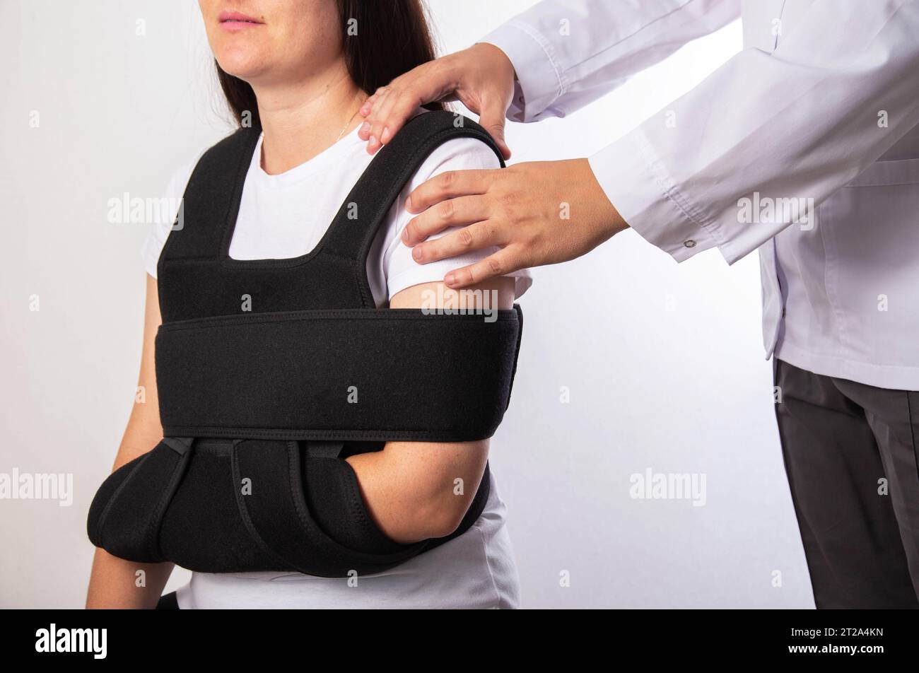 A doctor traumatologist examines a girl patient after a shoulder joint injury. Shoulder bandage. Rehabilitation after injury. Stock Photo