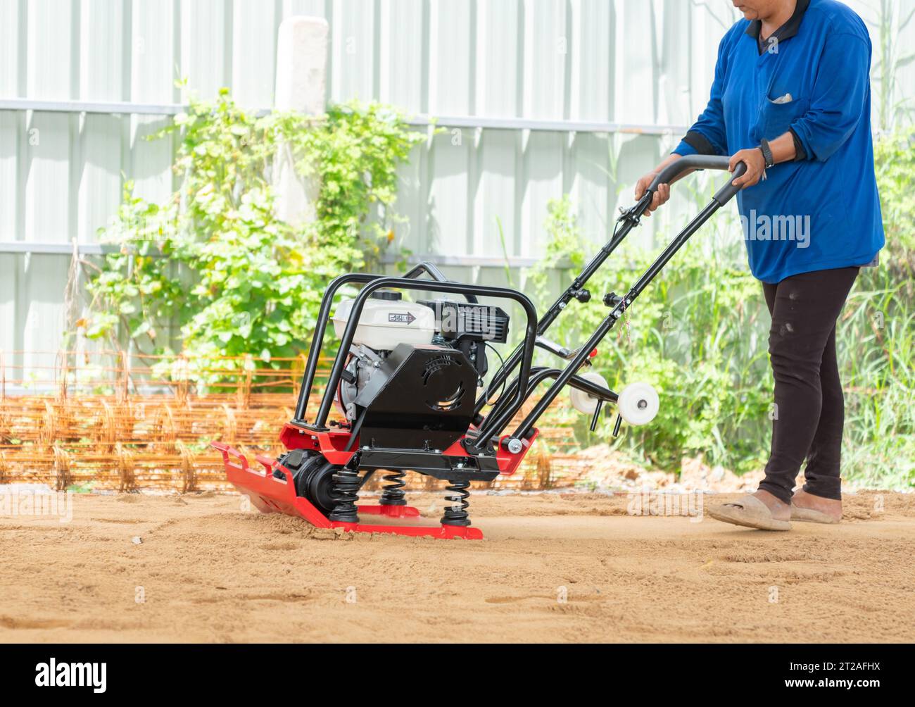 Worker in use vibratory plate compactor for compaction sand in
