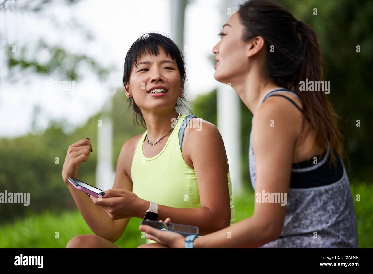 two happy young asian women female friends in sportswear relaxing chatting outdoors Stock Photo