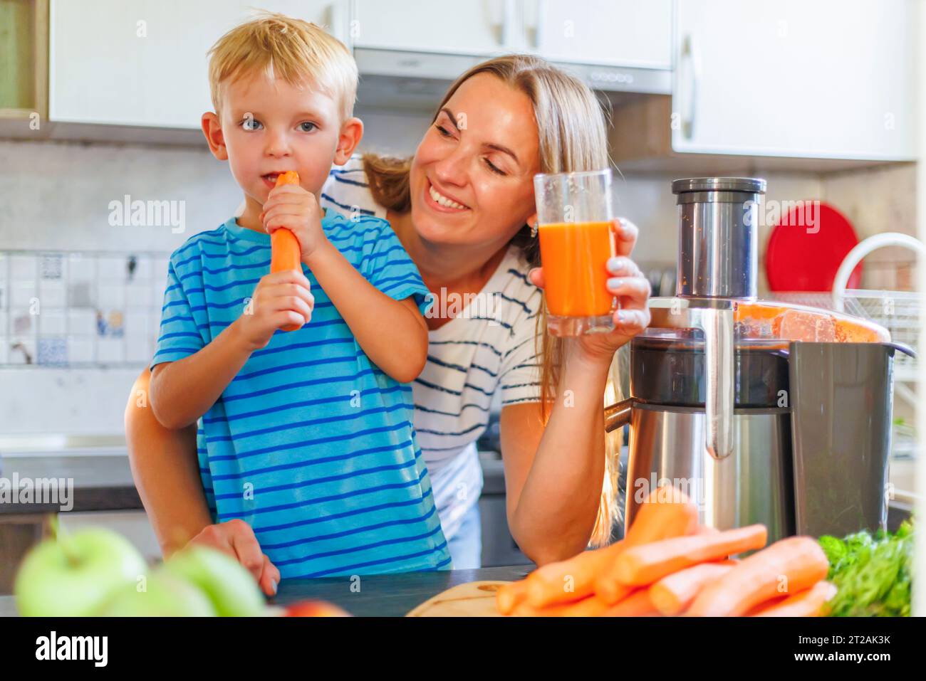 Mom and son drink fresh carrot juice squeezed using juicer in kitchen at home Stock Photo