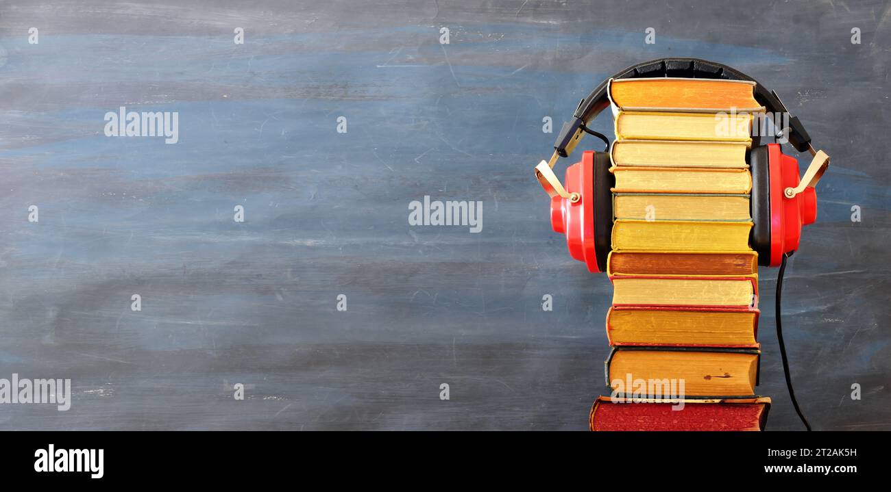 Relaxing with audiobooks concept with heap of books and vintage headphones. Dark background with large copy space. Stock Photo