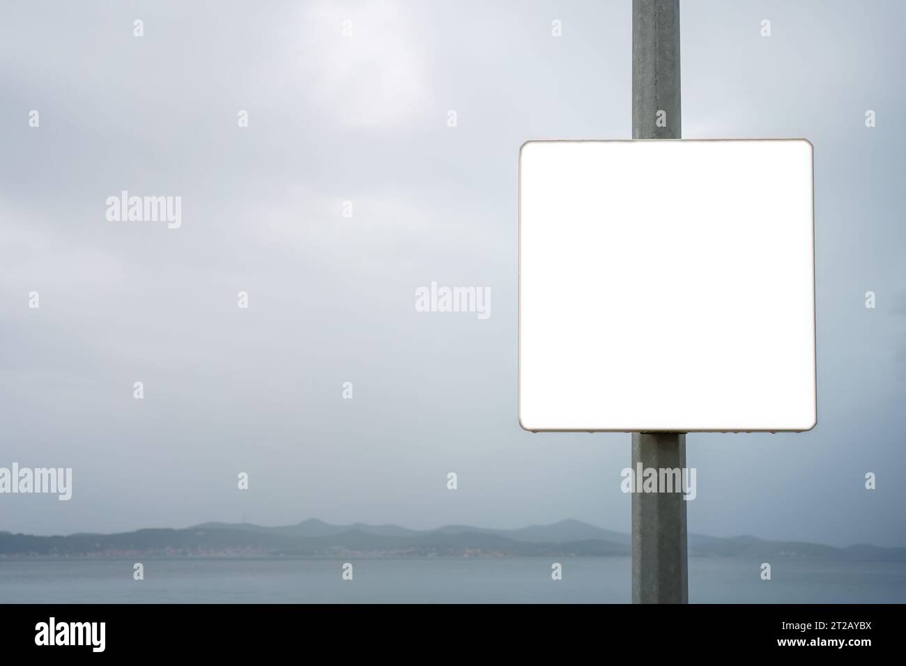 Close up of empty white sign next to the sea on overcast day. Stock Photo