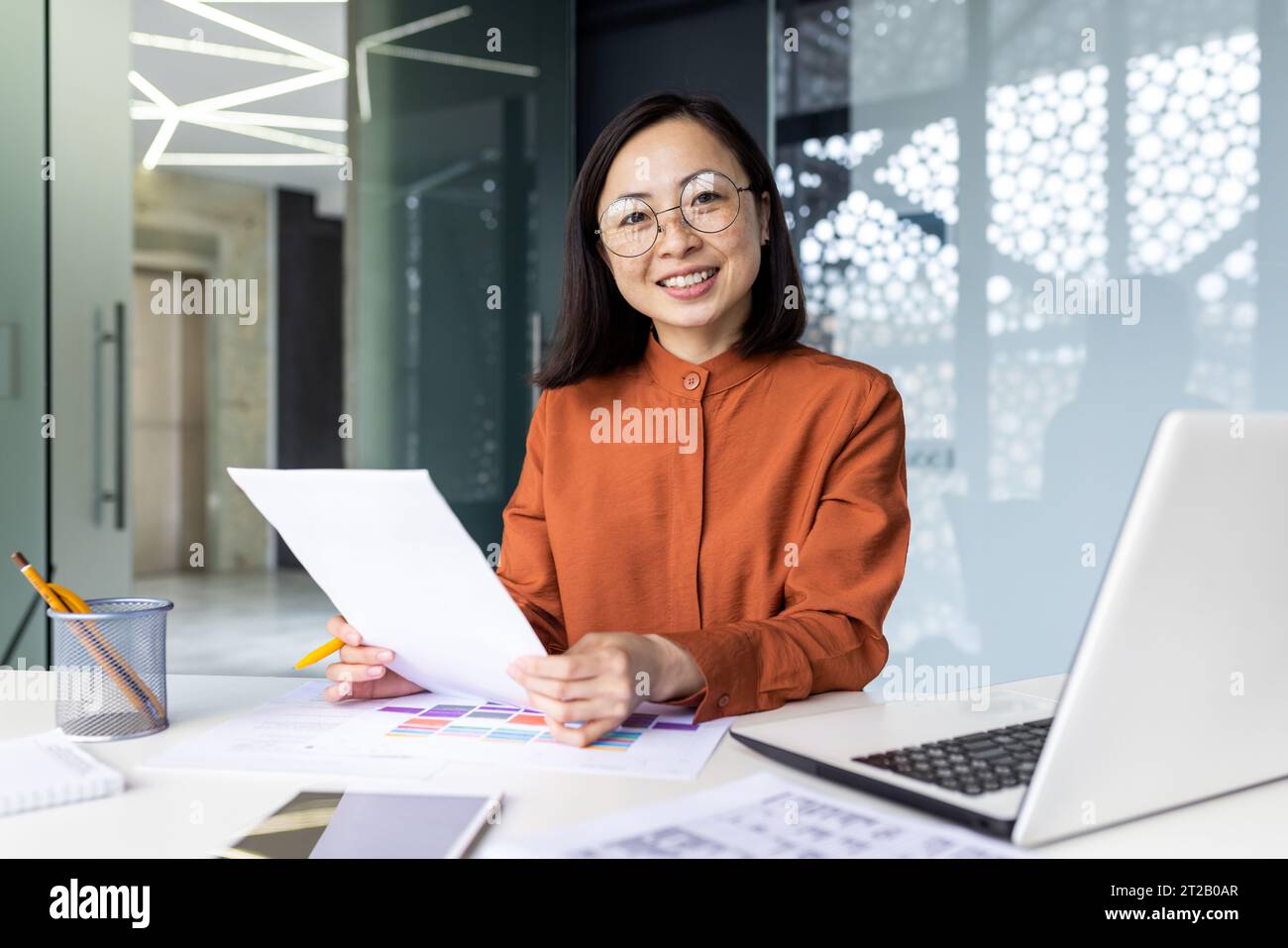 Successful Asian woman doing paperwork inside the office, businesswoman holding documents, reports and papers in her hands, smiling and looking at the Stock Photo