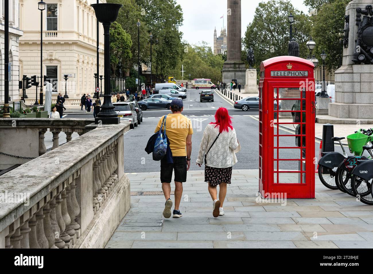 Rear view of a middle aged couple walking near Pall Mall , the woman has bright red hair which matches the colour off a London telephone next to her Stock Photo