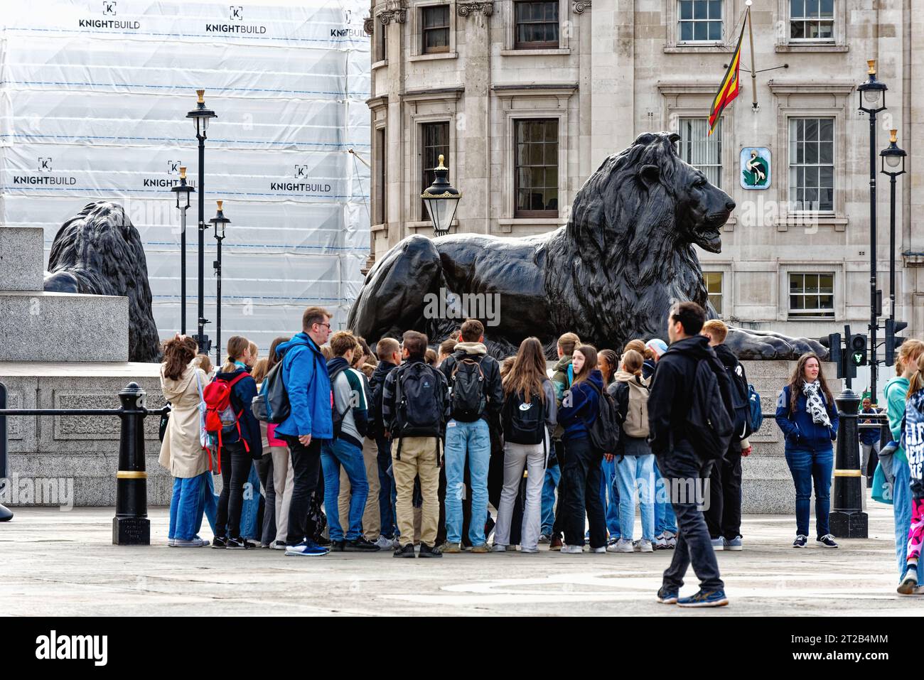 A group of teenage tourists gathered around one of the Trafalgar Square lions, Central London England UK Stock Photo