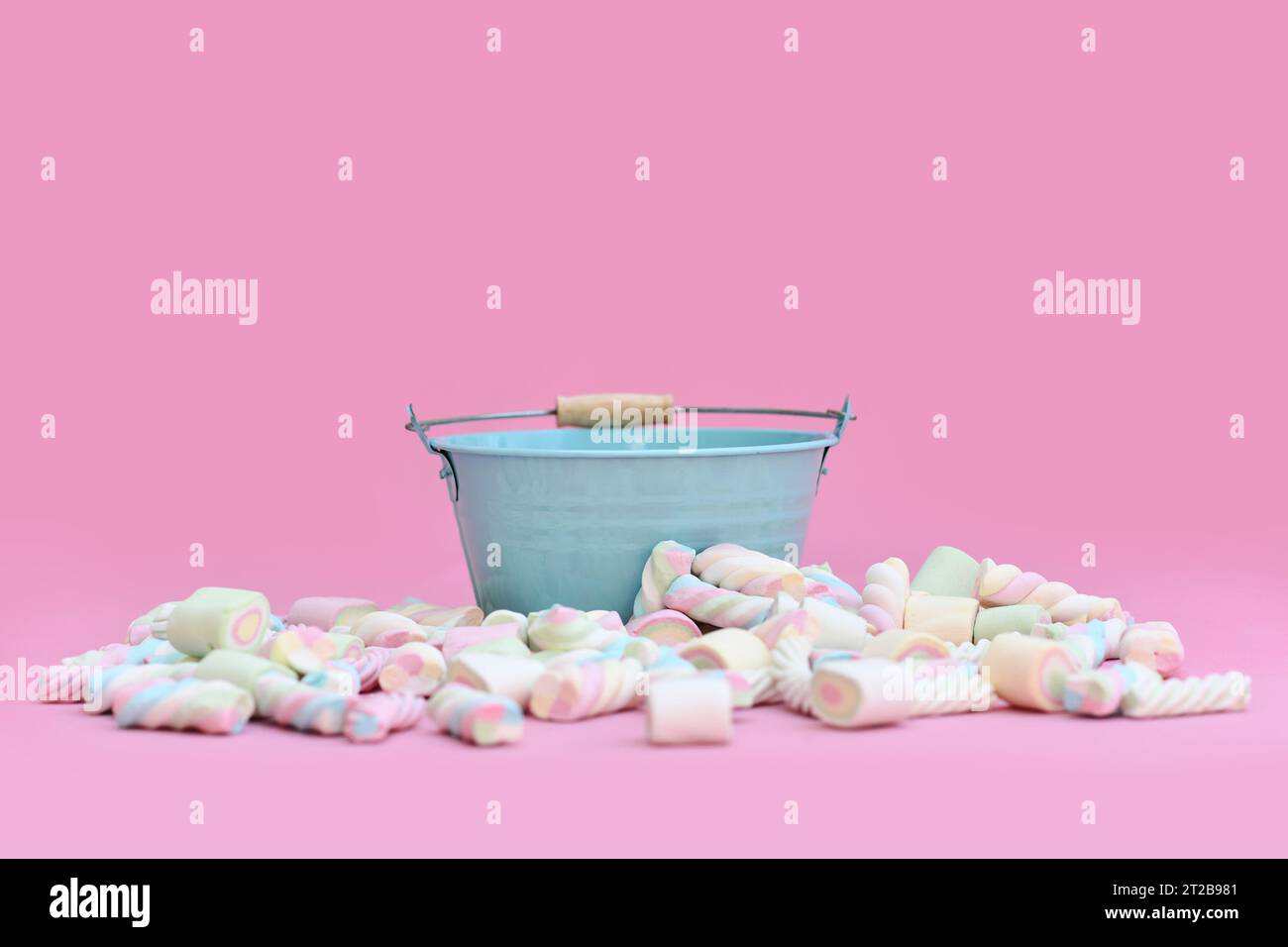 Empty blue bucket surrounded by marshmallow sweets in front of pink