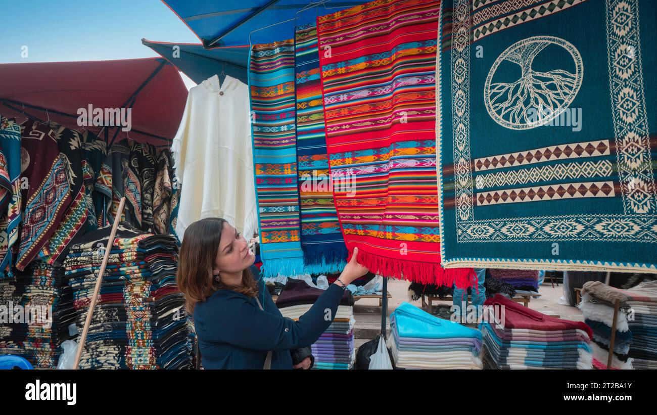 Beautiful young Latin American woman buying multicolored fabrics in the Plaza de los Ponchos in the city of Otavalo - Ecuador Stock Photo