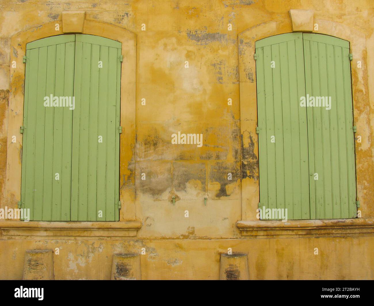 Pistachio green shutters covering windows on a bright yellow wall in Arles. - Stock Image