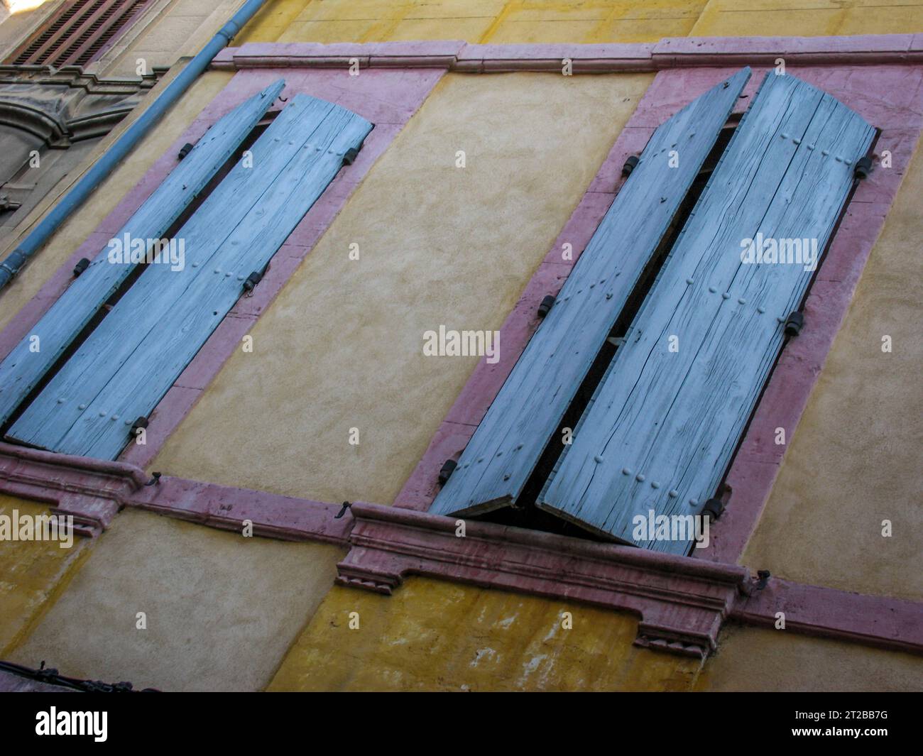 Colorful shutters covering windows on a naples yellow wall in Arles. - Stock Image