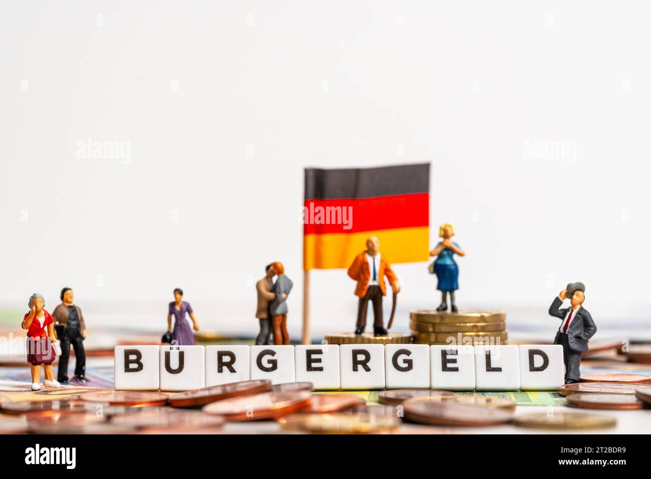 Augsburg, Bavaria, Germany. 16th Oct, 2023. Letter cubes form the word Bürgergeld. Miniature figures on coin money stack next to euro cash bills and a German national flag. Symbol picture citizen money instead of Hartz IV *** Buchstabenwürfel bilden das Wort Bürgergeld. Miniaturfiguren auf Münzgeld Stapel neben Euro Bargeld Scheinen und einer deutschen Landesflagge. Symbolbild Bürgergeld statt Hartz IV Credit: Imago/Alamy Live News Stock Photo