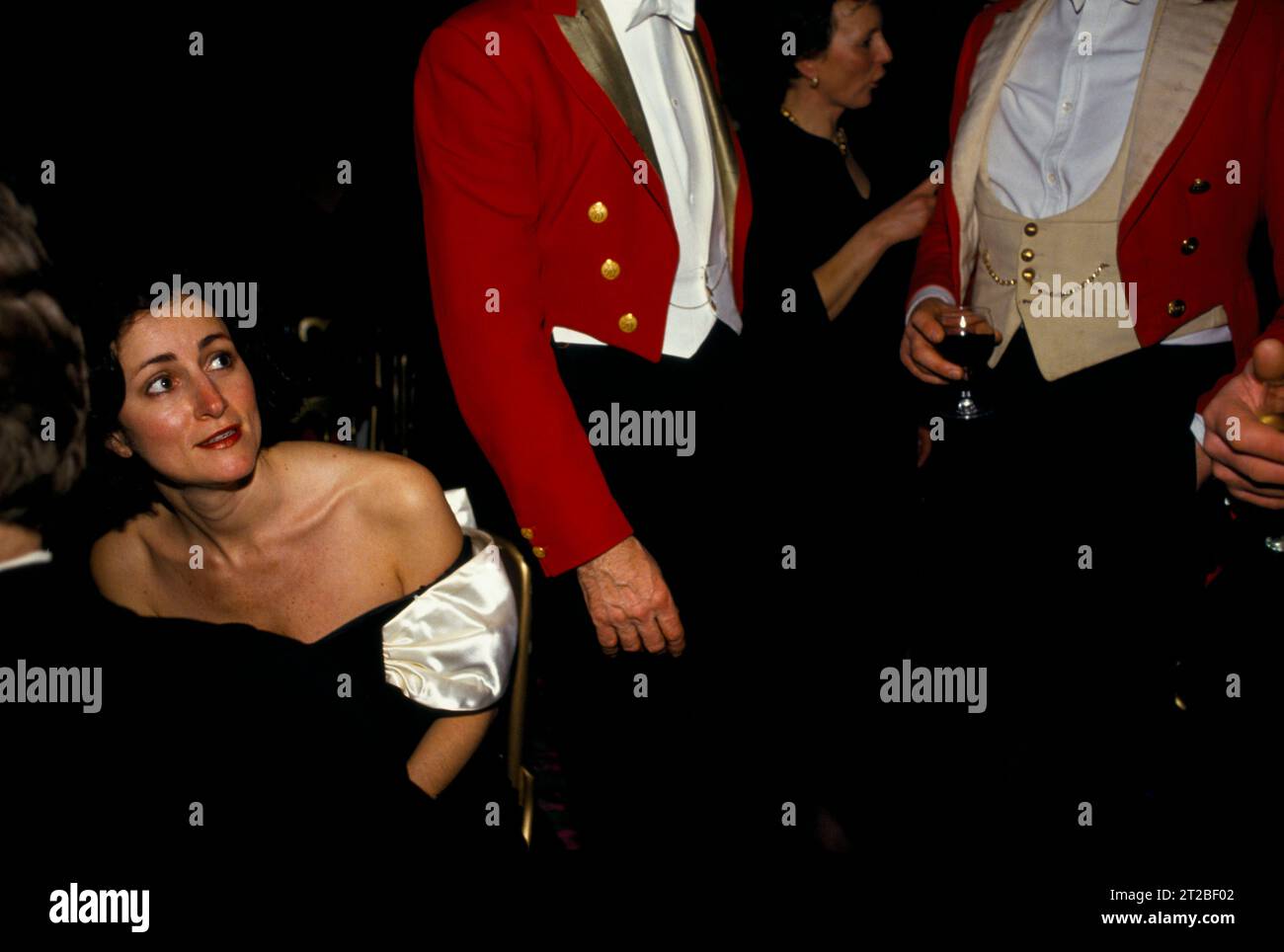 1980s Hunt Ball at Tysoe Manor, celebrates the end of the hunting season. A woman in an off the shoulder strapless black ball gown dress and two Masters of Foxhounds chatting wearing their traditional hunting pink evening formal attire.  Tysoe, Warwickshire, England April 1982. 1980s UK HOMER SYKES. Stock Photo