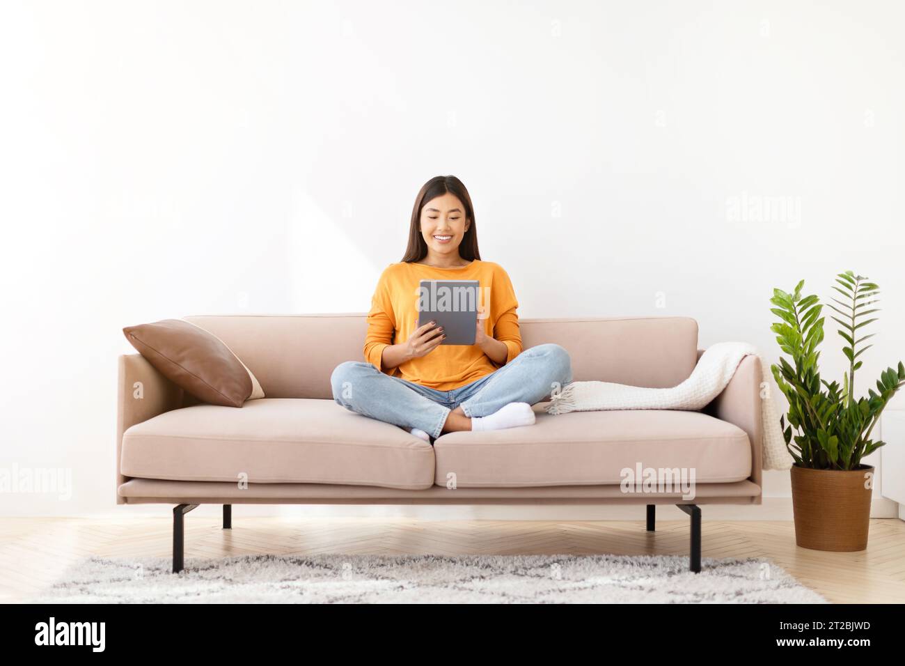 Happy asian woman sitting on couch, using tablet at home Stock Photo ...