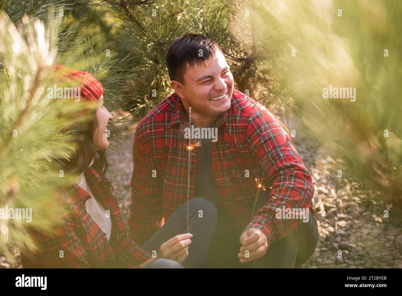 Through green needles of pine trees, young happy couple in red