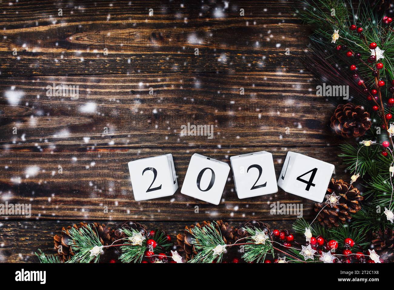New Year's 2024 wood calendar blocks. Christmas tree lights, pine branches, red winter berries and snow over wooden table background. Top view with co Stock Photo