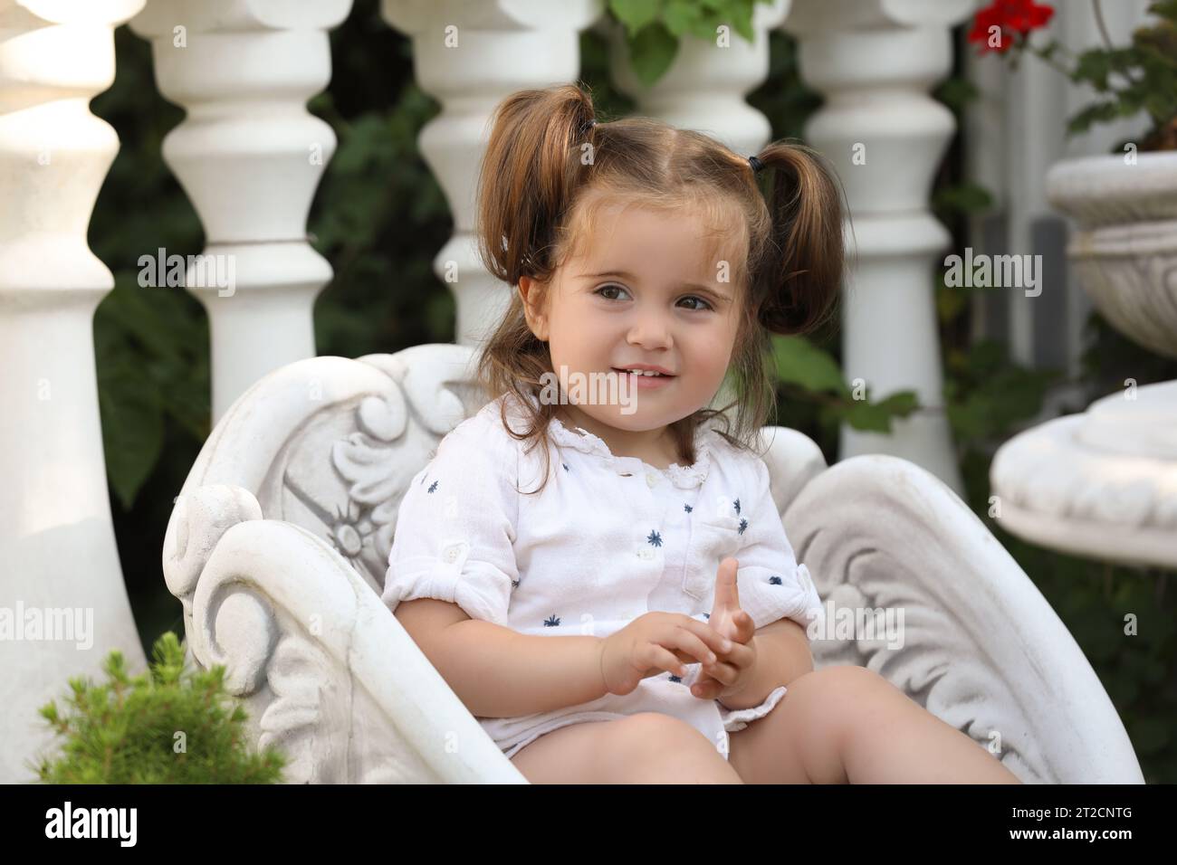 Cute little girl in white dress sitting in chair outdoors Stock Photo ...