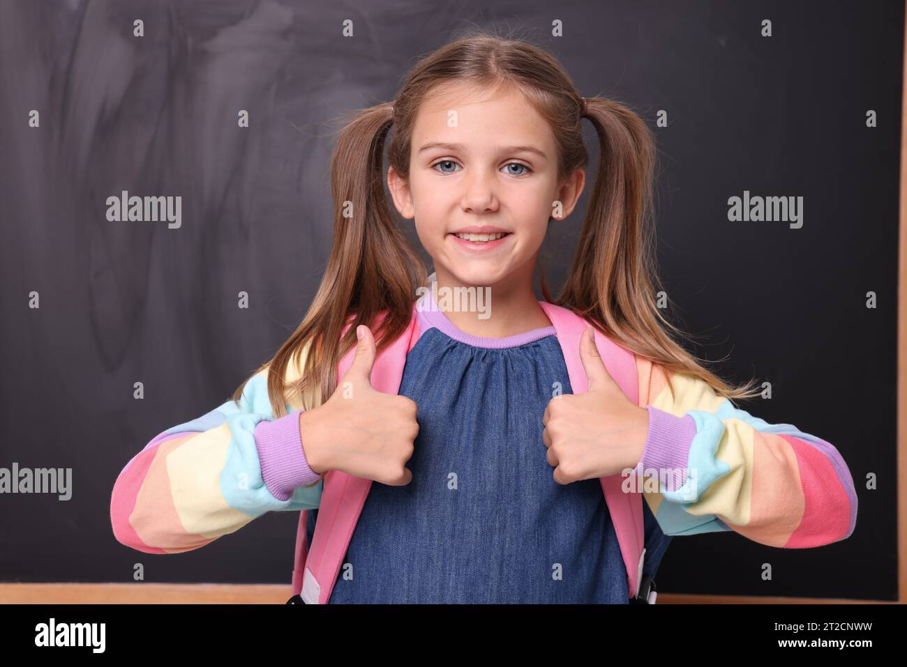 Smiling schoolgirl showing thumbs up near blackboard Stock Photo - Alamy