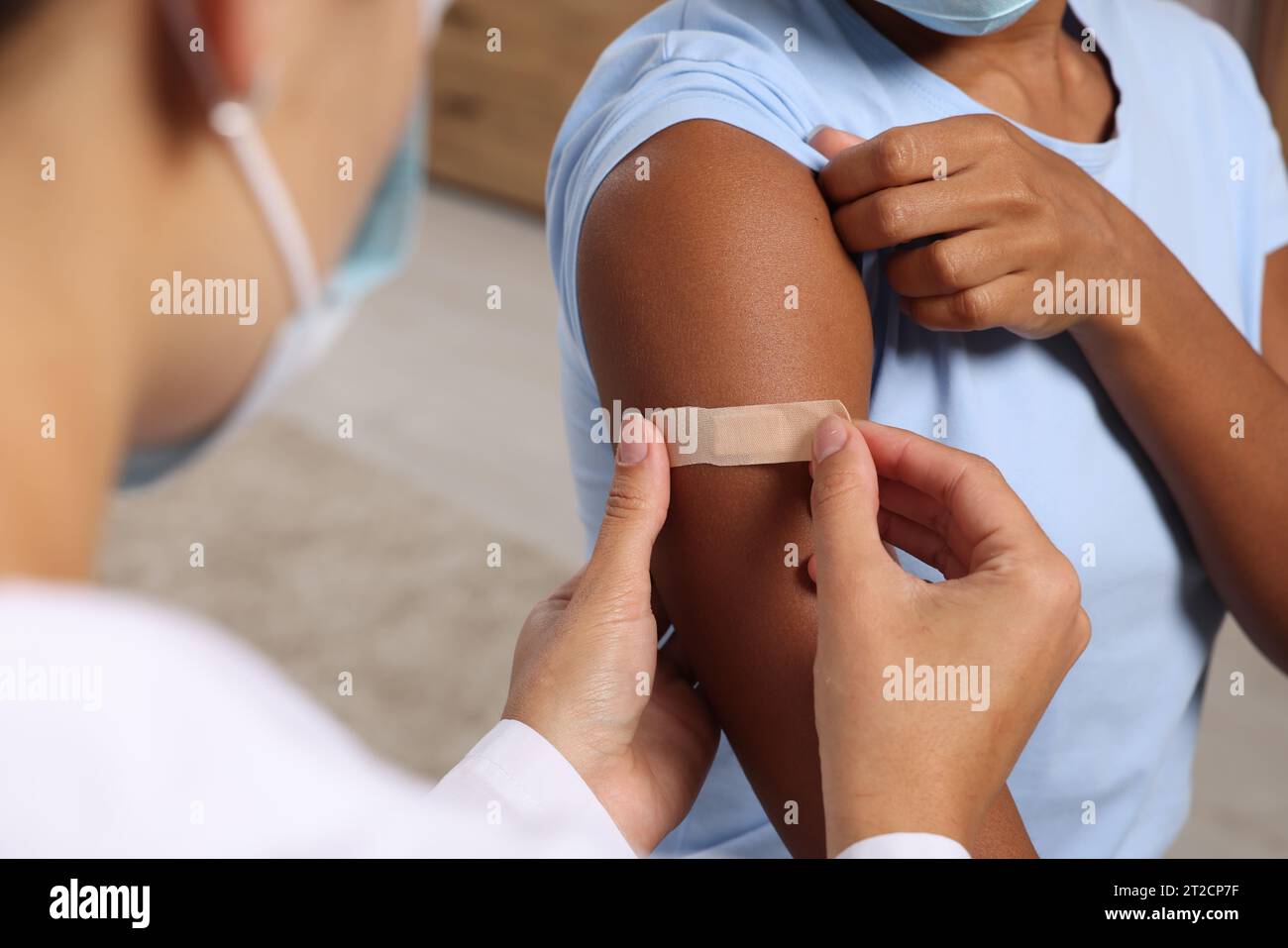 Doctor putting adhesive bandage on young woman's arm after vaccination indoors, closeup Stock Photo