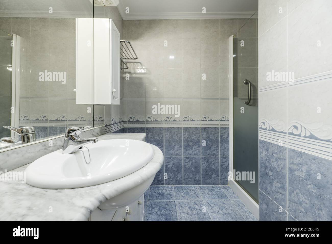 Bathroom of a home with two-color tiles divided by a marine border, a frameless mirror Stock Photo