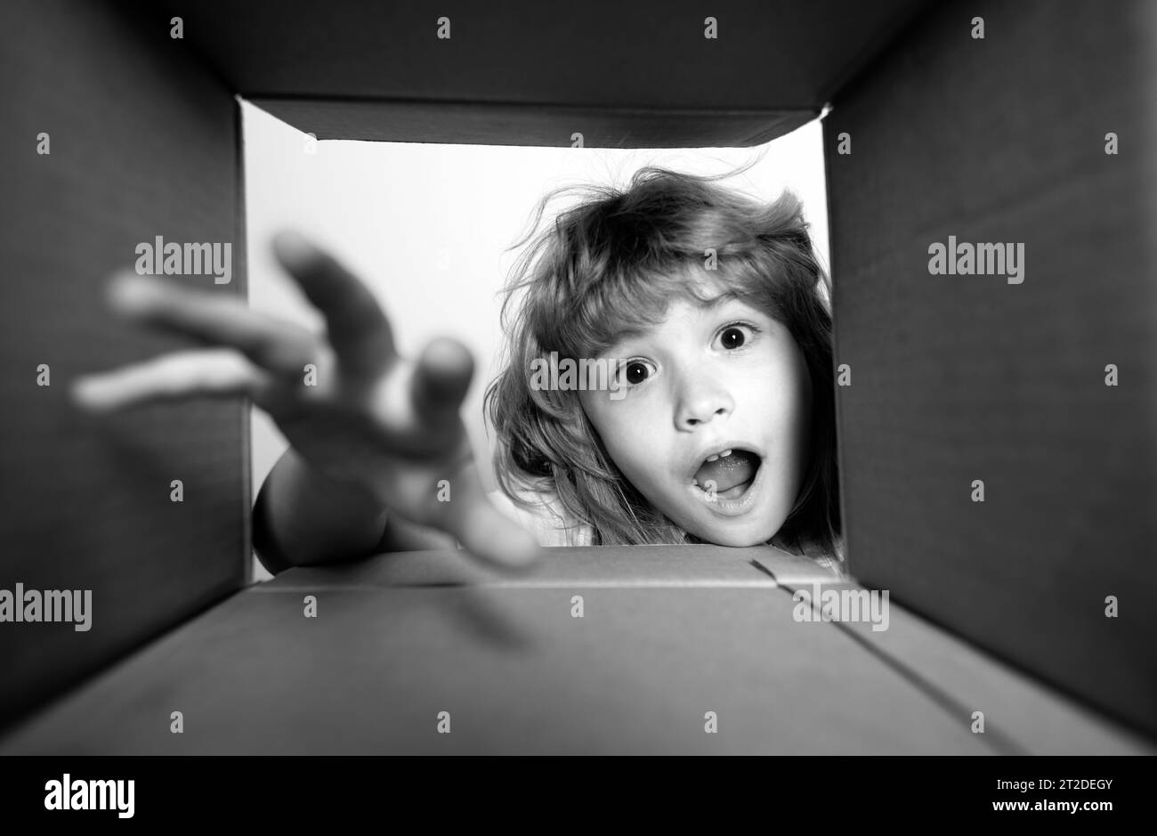 Kid unpacking and opening carton box, and looking inside with surprise face. Child boy looking surprised into a gift. Stock Photo