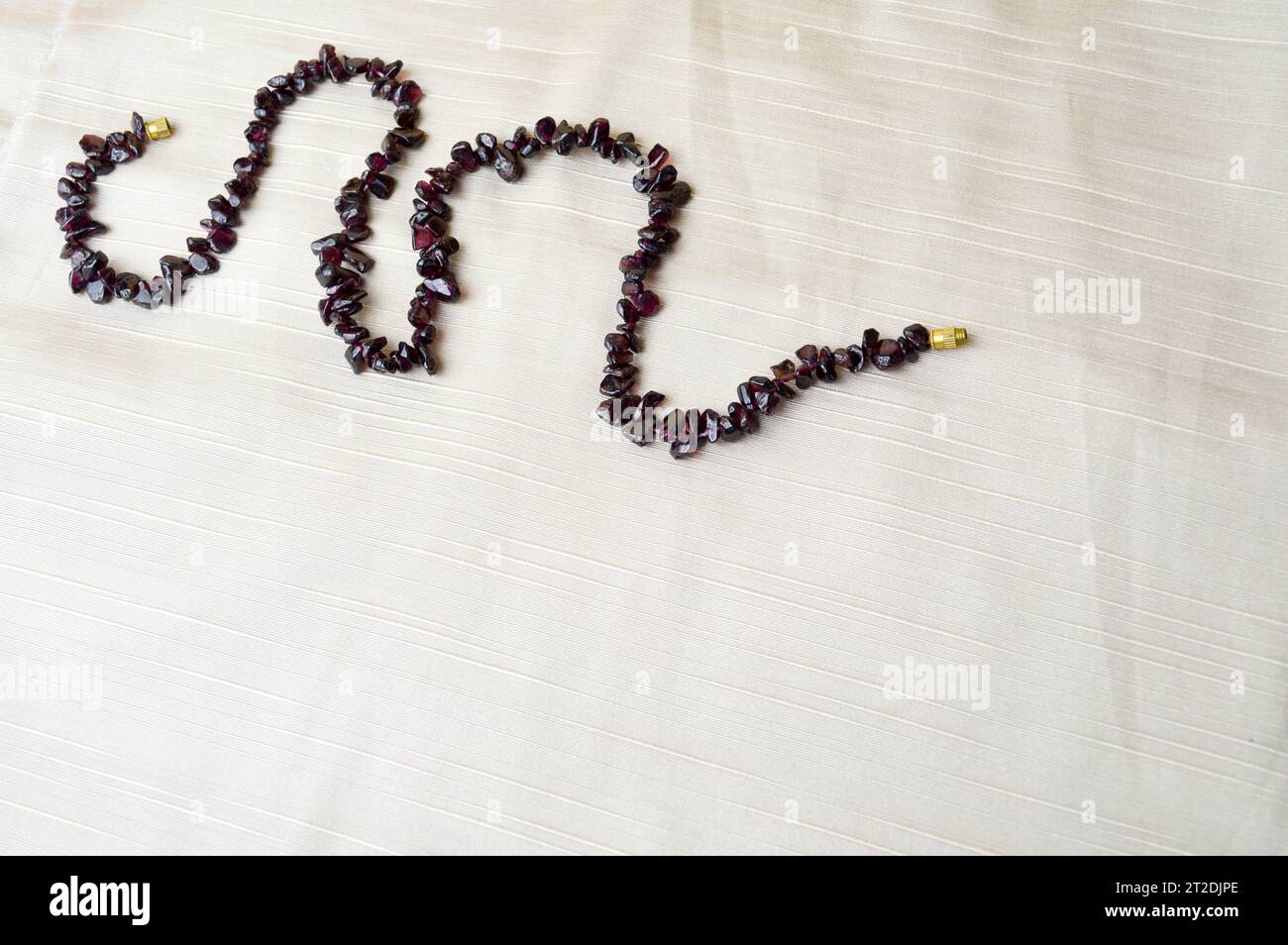 Women's beautiful beads, a necklace of brown dark stones, amber arranged by a snake, a wave against a background of beige cloth and a place for text. Stock Photo