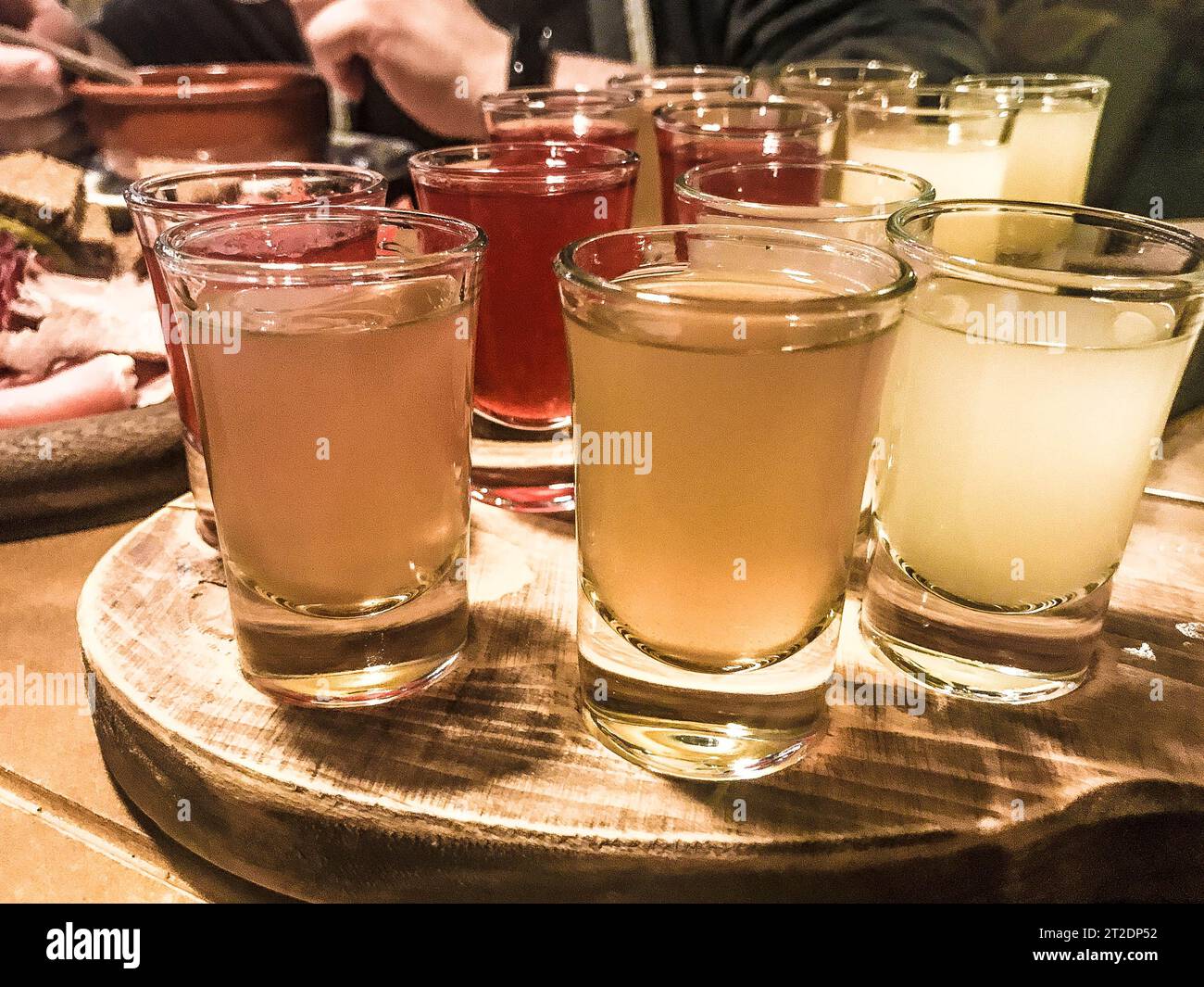 A set of lots of delicious yellow orange red glasses, shots with strong alcohol, vodka, filling, brandy on wooden stands on a table in a cafe, bar, re Stock Photo