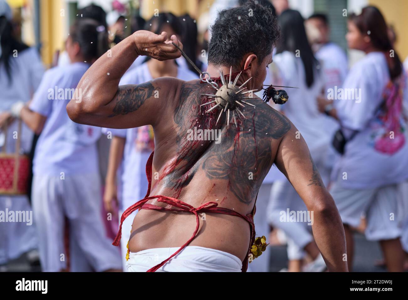 During the Vegetarian Festival in Phuket Town, Thailand, a participant self-flagellates with a spiked iron ball, causing bleeding wounds on his back Stock Photo