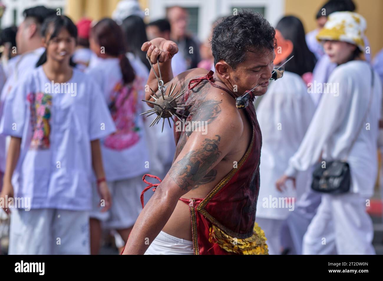 During the Vegetarian Festival in Phuket Town, Thailand, a participant self-flagellates with a spiked iron ball, causing bleeding wounds on his back Stock Photo