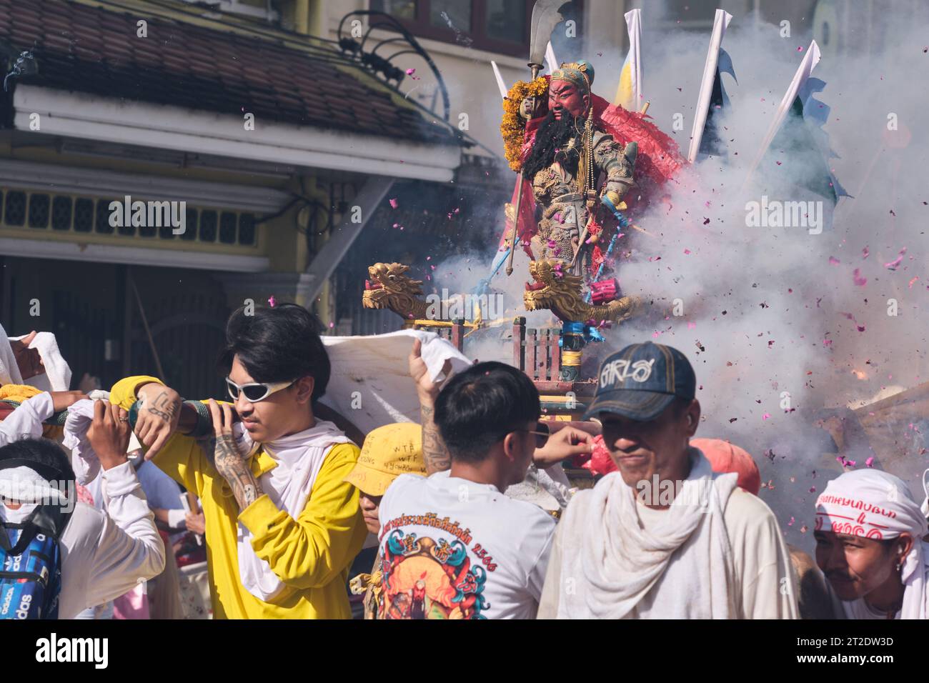 A street procession in Phuket Town during the festival, with crowds parting around mah song devotees while firecrackers explode in the foreground