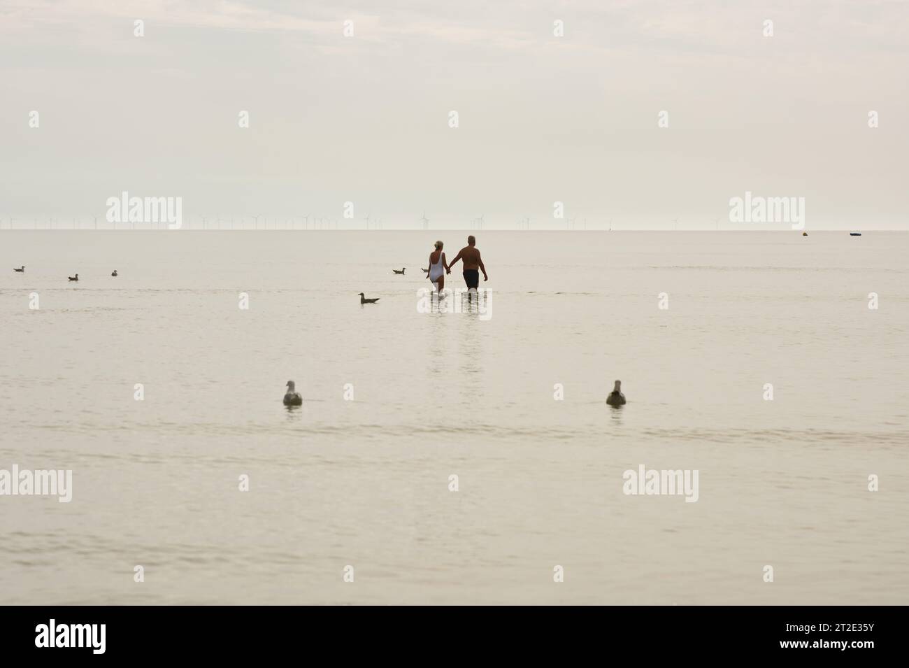 Man and woman holding hands and walking in a very calm sea with white cloud and mist. Littlehampton, West Sussex, England Stock Photo