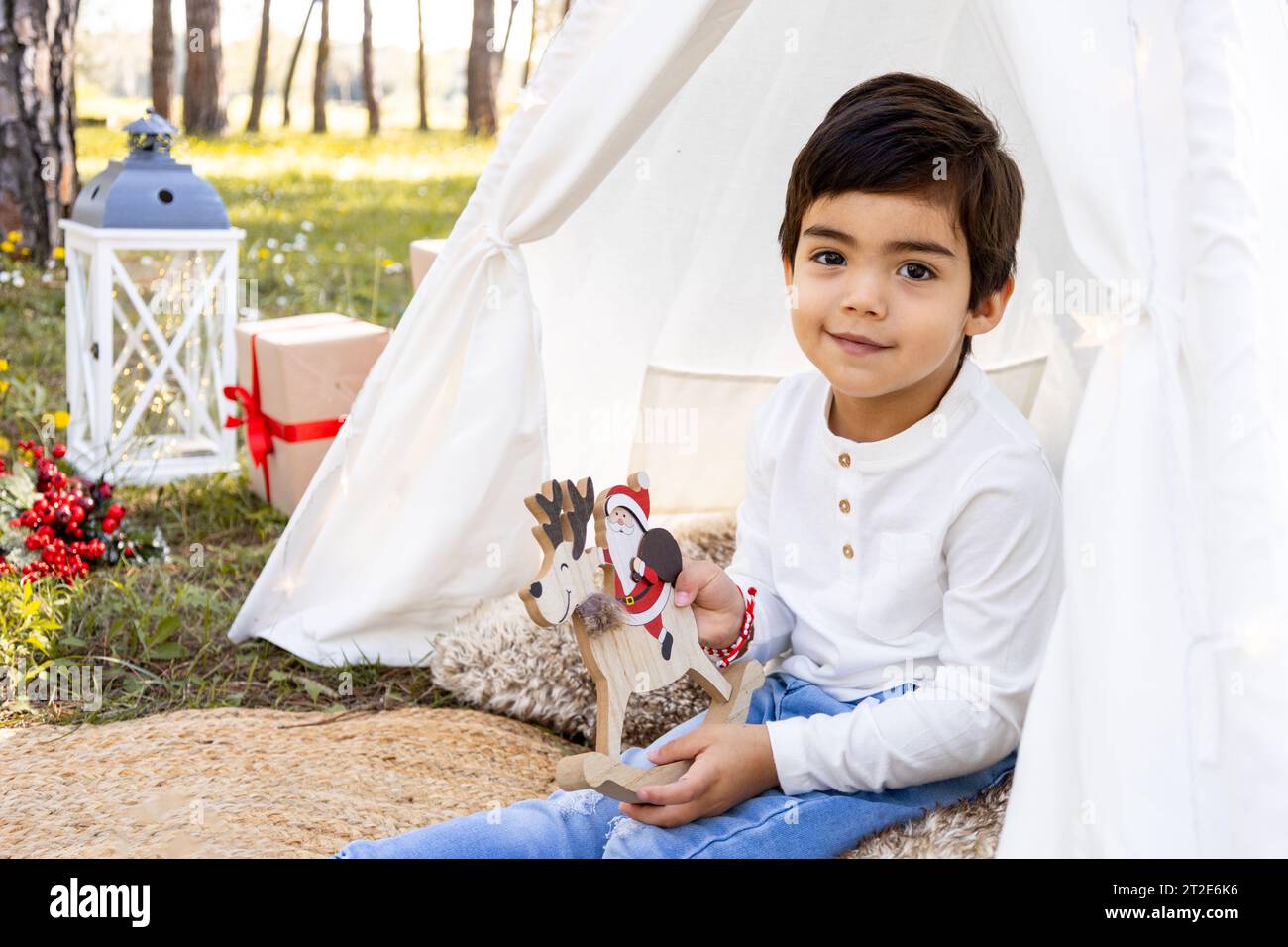 Smiling child boy playing with Christmas decoration in outdoor teepee tent. Winter family photoshoot in the forest. Stock Photo