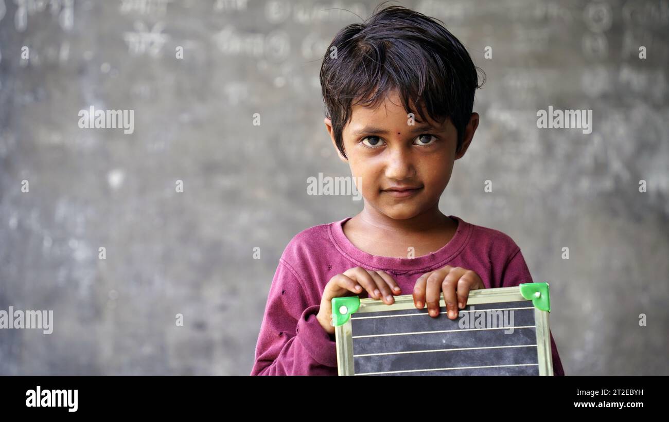 Portrait of happy cute little indian girl in school uniform holding blank slate, Adorable elementary kid showing black board. child education concept. Stock Photo