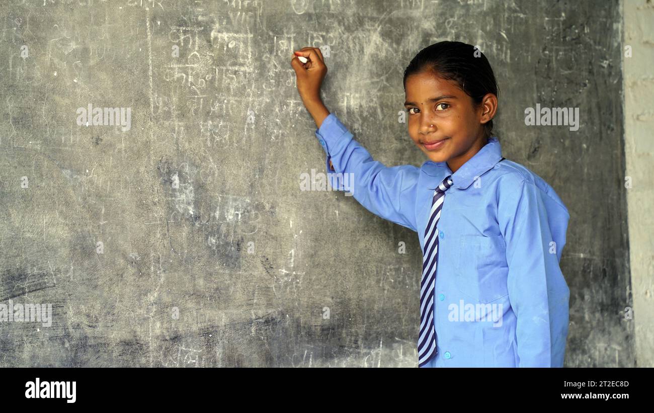 Happy Indian school girl child standing in front of black chalkboard