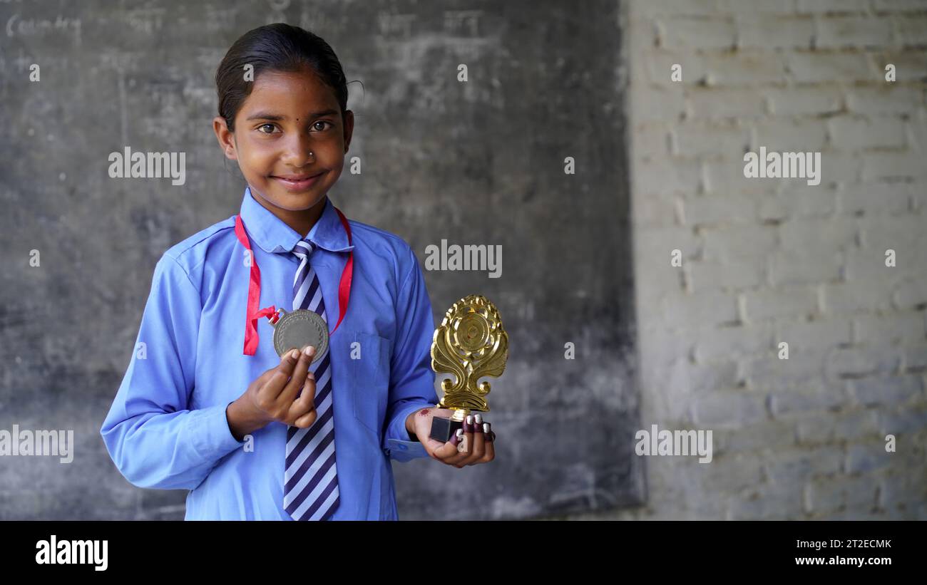 Portrait of a Happy School girl wearing school uniform celebrating victory trophy in hand. Education concept. skill india. child dreams Stock Photo