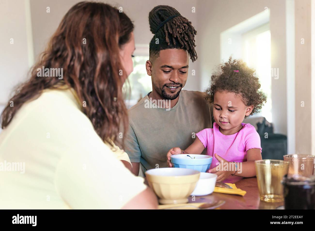 A heartwarming scene of a Caucasian mother, African father, and their daughter enjoying breakfast together in the living room, showcasing the beauty o Stock Photo