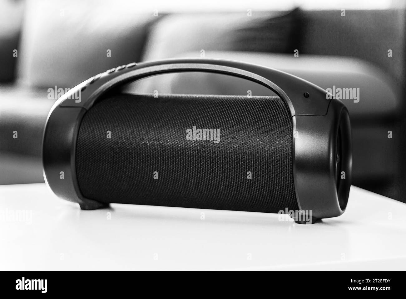 Portable wireless speaker on a table indoors against the background of a sofa, black and white photo, shallow depth of field Stock Photo