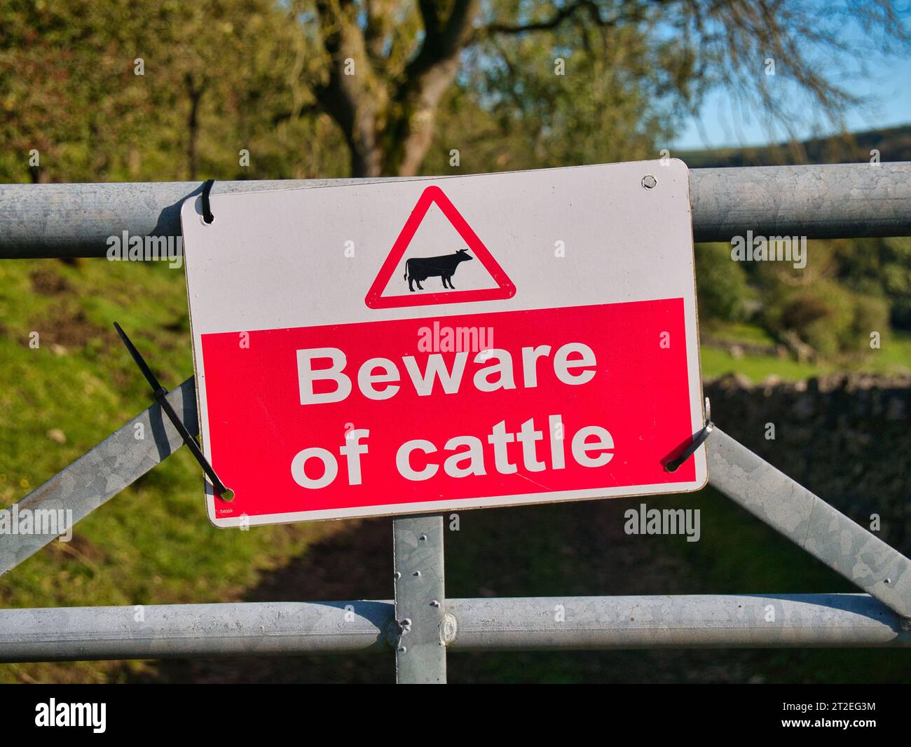 A rectangular red and white sign fixed to a metal farm gate advising ...