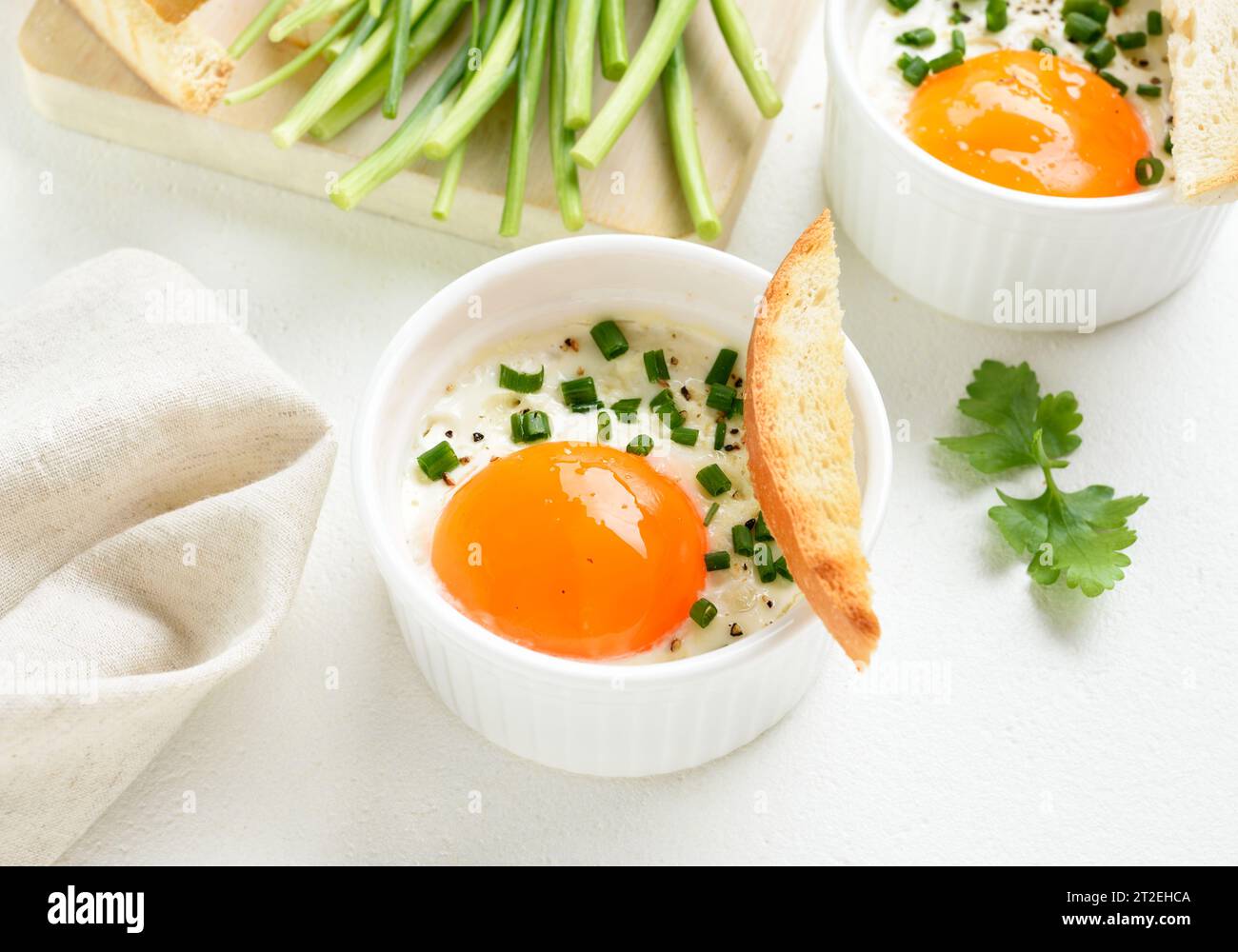 Baked eggs (Eggs en cocotte) with cream, сheese and green onion in