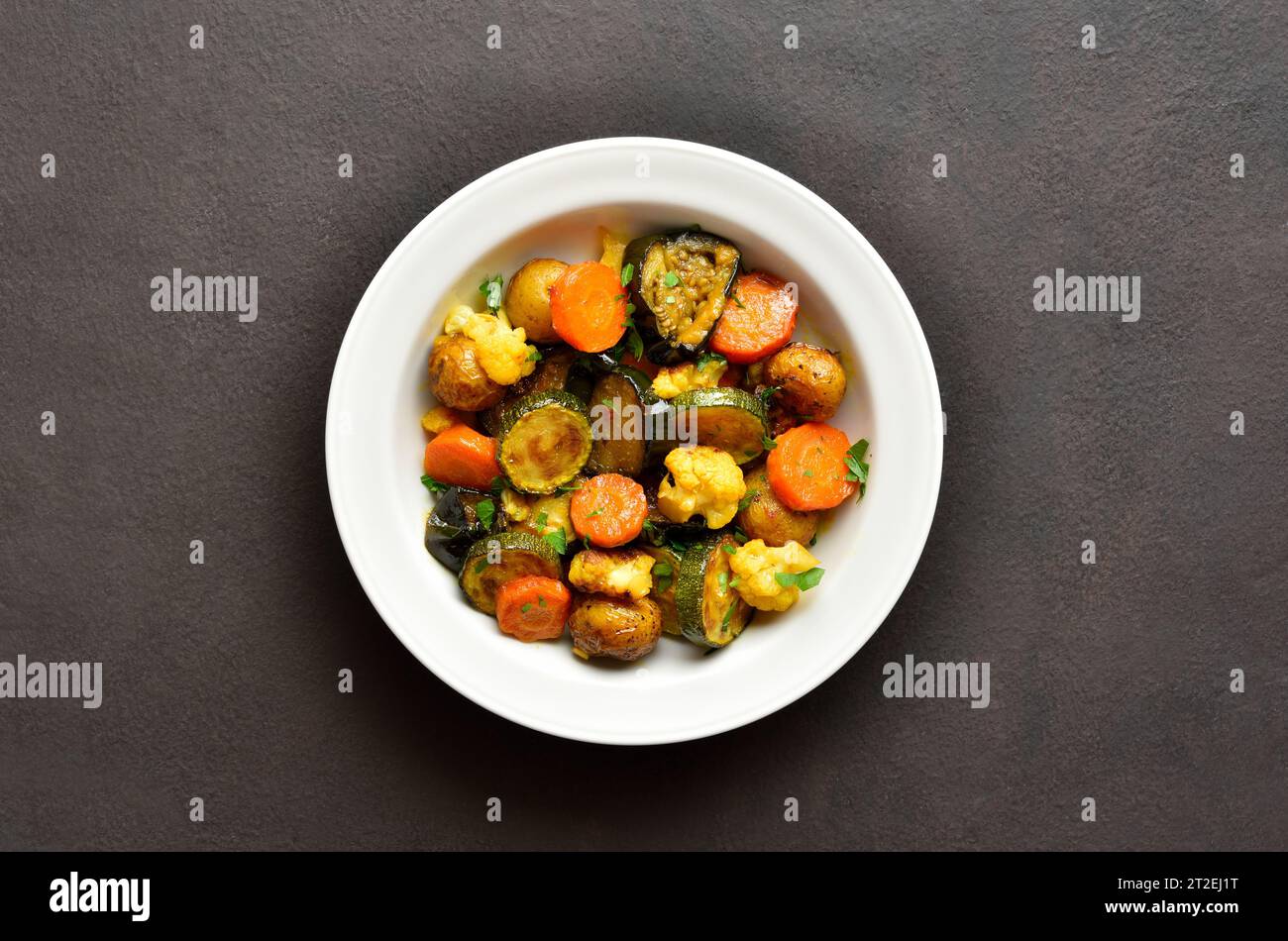 Stewed vegetables on white plate over dark background with copy space. Top view, flat lay Stock Photo