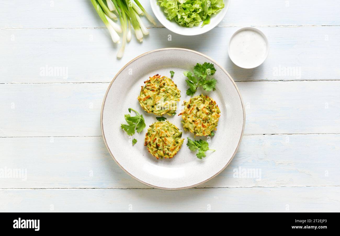 Vegetable vegetarian zucchini pancakes with green onion on plate with sauce over light wooden backround. Top view, flat lay Stock Photo