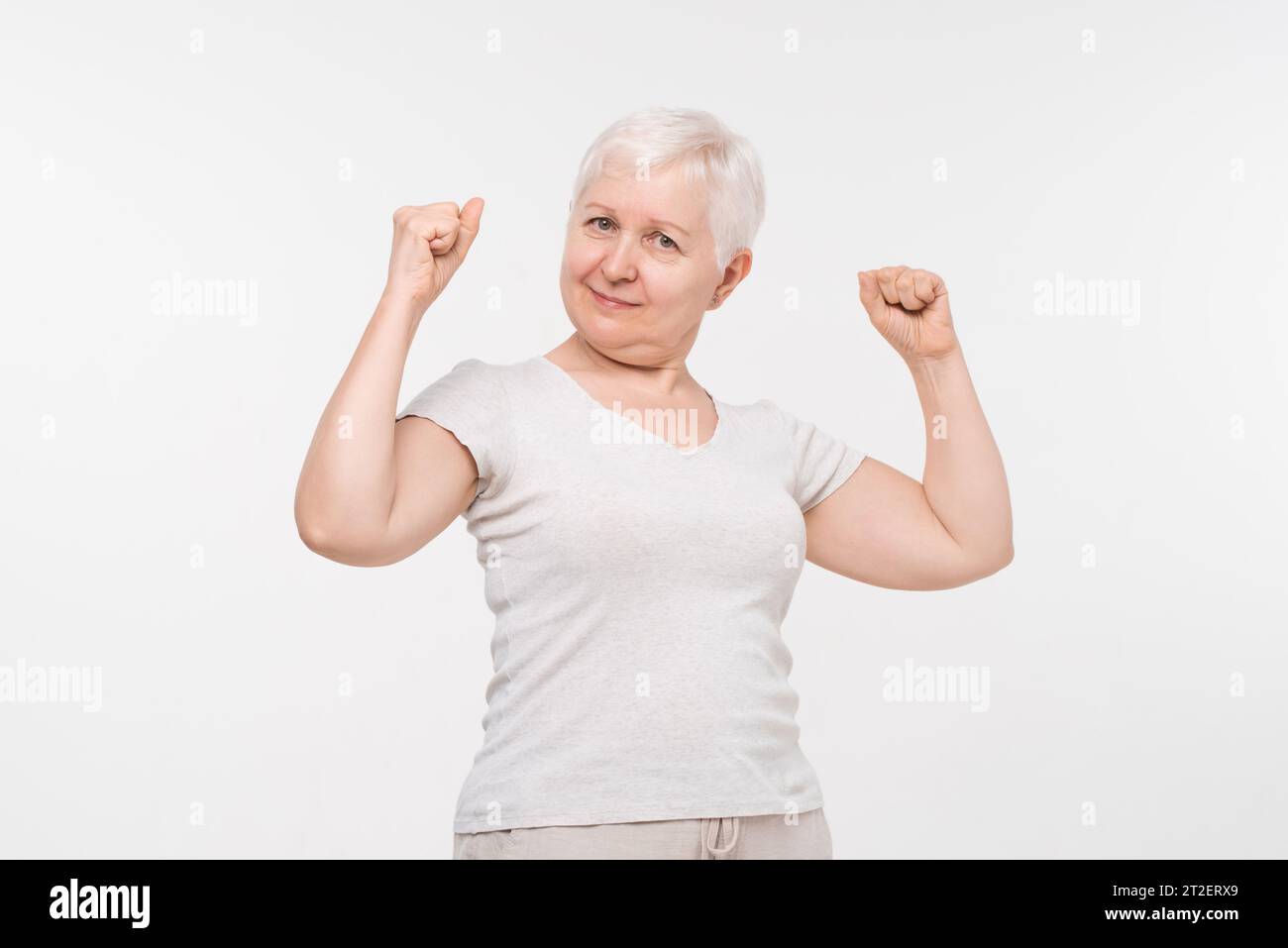 Portrait of happy healthy active senior elderly woman smiling and raising fists in isolated white background studio shot, health care and insurance co Stock Photo