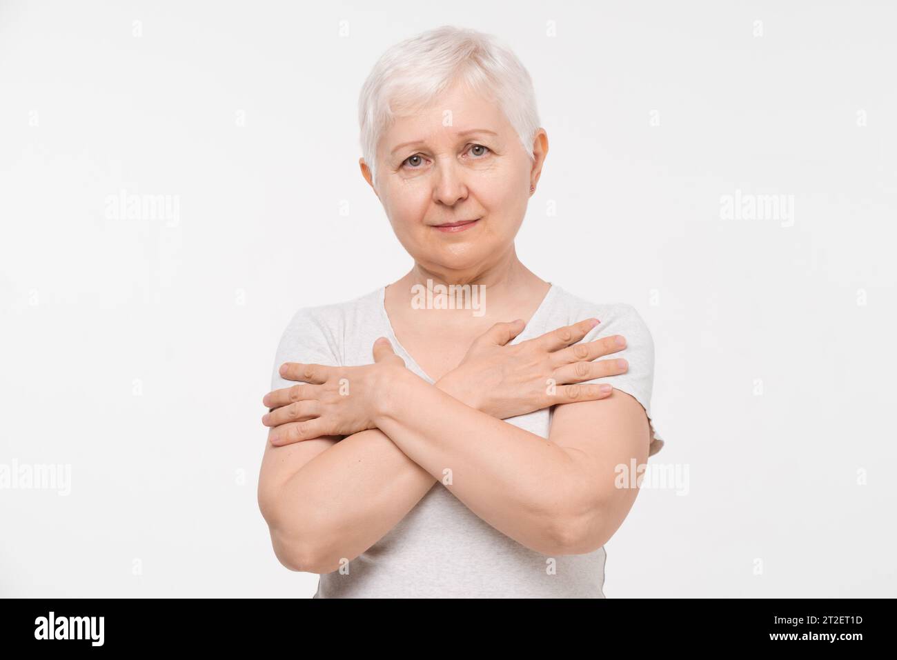 Portrait of healthy senior elderly woman holding hands on chest in isolated white background studio shot Stock Photo