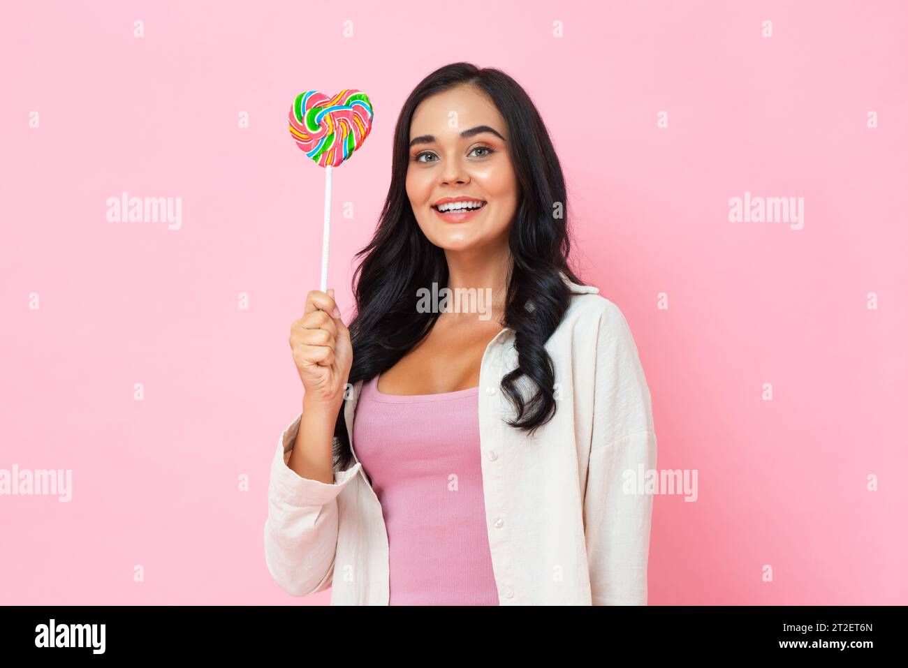 Young pretty positive woman holding lollipop with smiling face in pink color isolated background studio shot Stock Photo